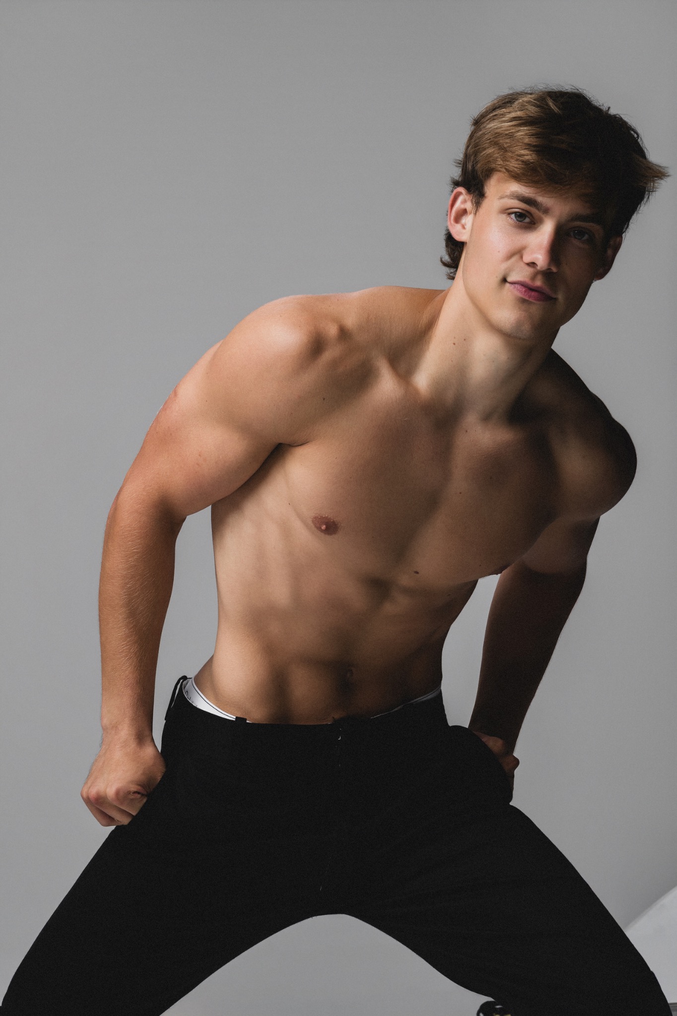 Andrew Ashley leaning forward in black trousers in a color studio portrait